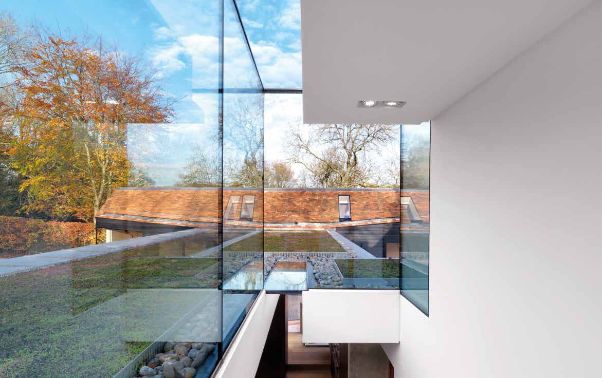 Angled frameless glass walls overlooking a planted roof and trees