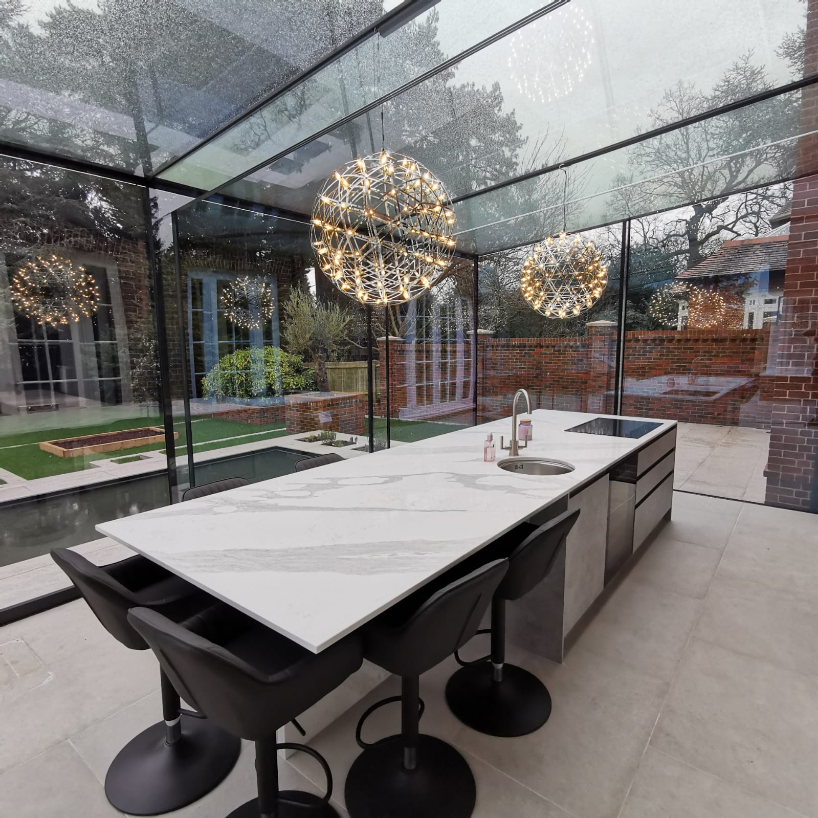 Glass-roofed kitchen-diner with an island, dining stools and views into a walled garden