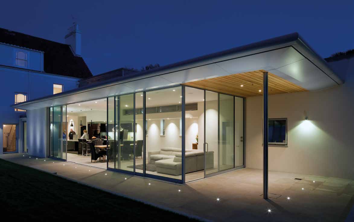Glass pavilion with frameless sliding doors opening onto a terrace at dusk
