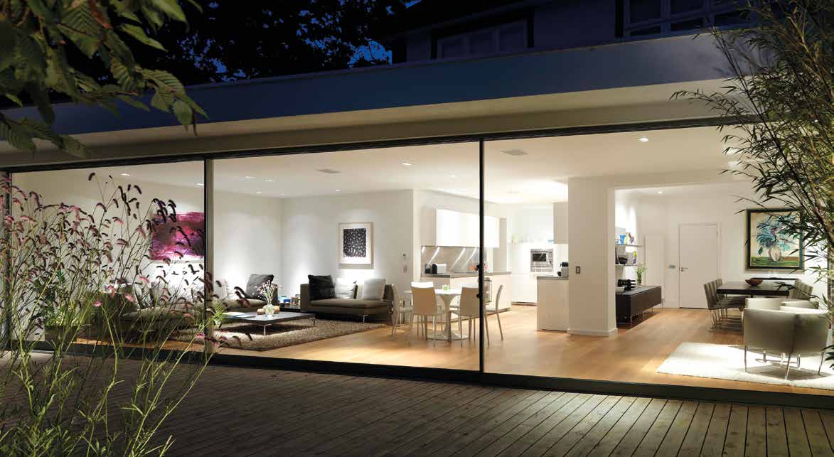 Slimline sliding glass doors revealing an illuminated open-plan living and kitchen space at night