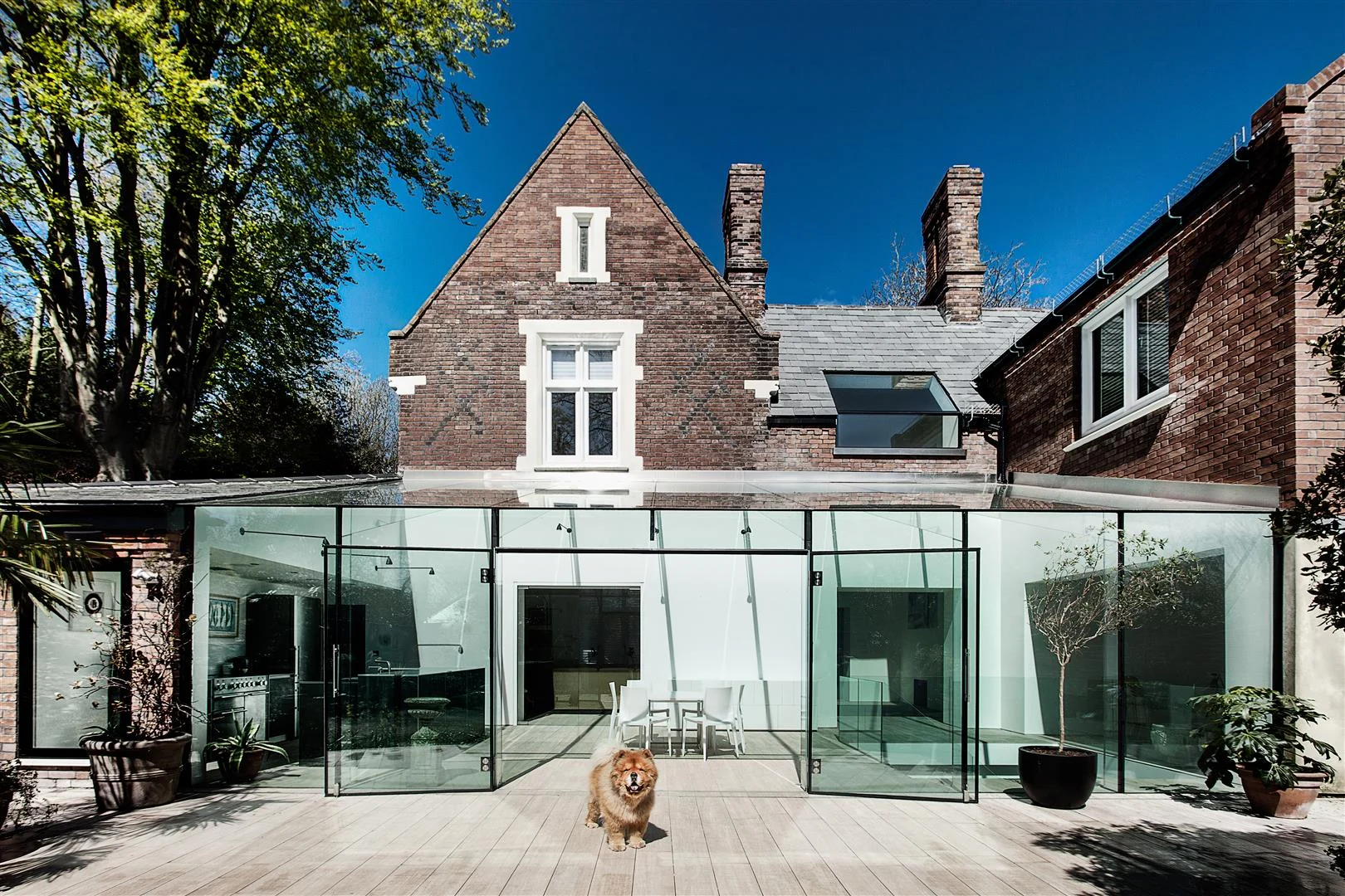 The Old Manor House red-brick exterior with a glass extension opening onto a terrace and a dog in the foreground