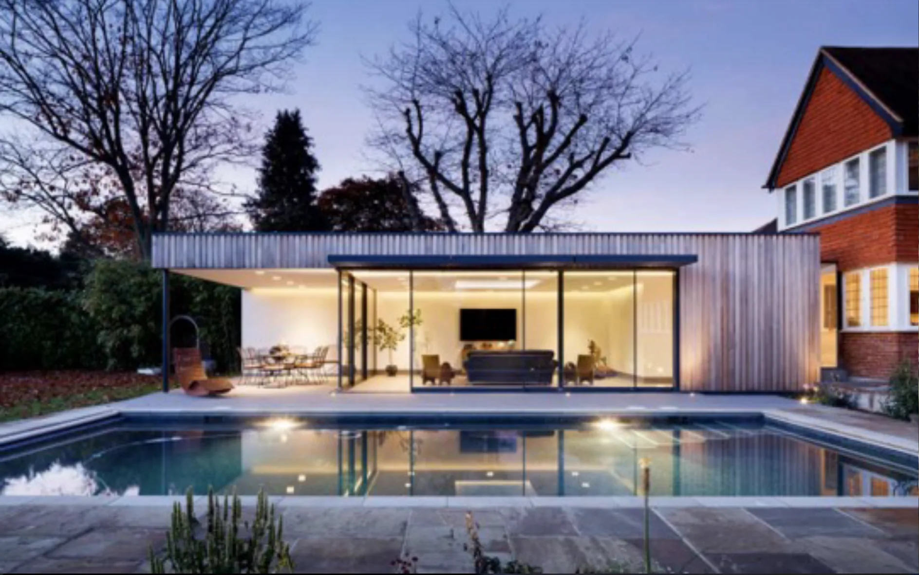 Illuminated glazed living space overlooking an outdoor swimming pool
